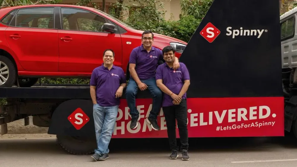 The three founders of Spinny sitting on a branded delivery truck.